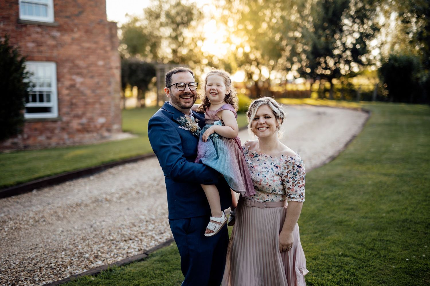 Wedding party posing outdoors at sunset against brick building and garden landscape.