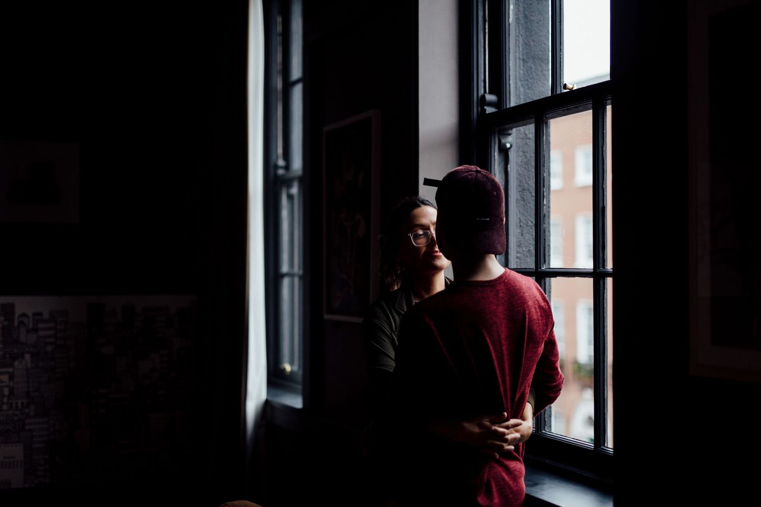 Silhouette of someone standing by large windows in a dark room.
