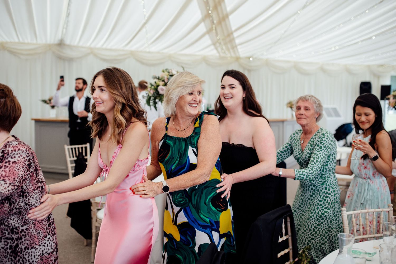 Wedding reception guests enjoying themselves under an elegant white tent marquee.