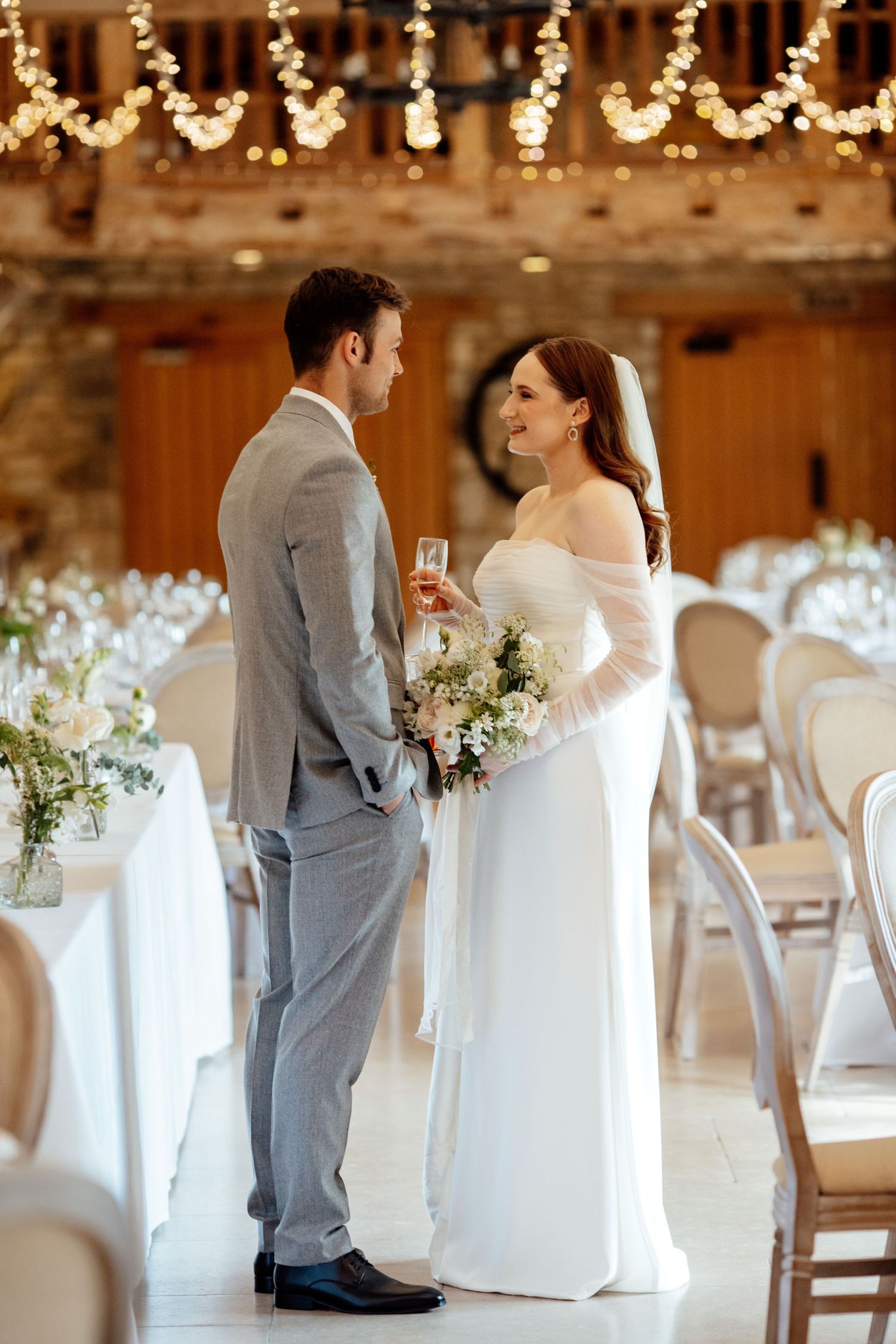 Couple sharing intimate moment in elegant reception venue decorated with string lights and floral arrangements.