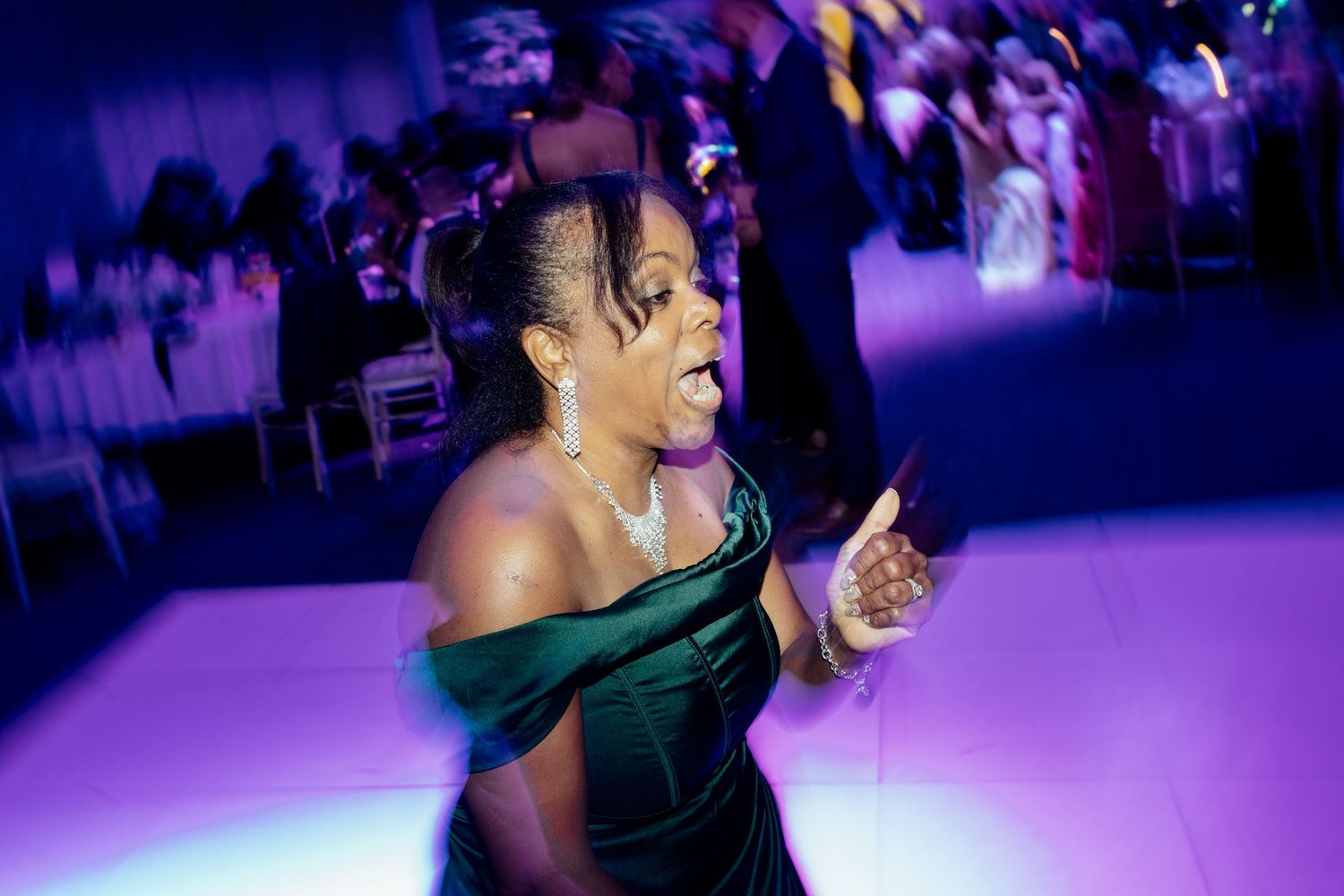 Wedding reception guests dancing and celebrating on a purple-lit dance floor.