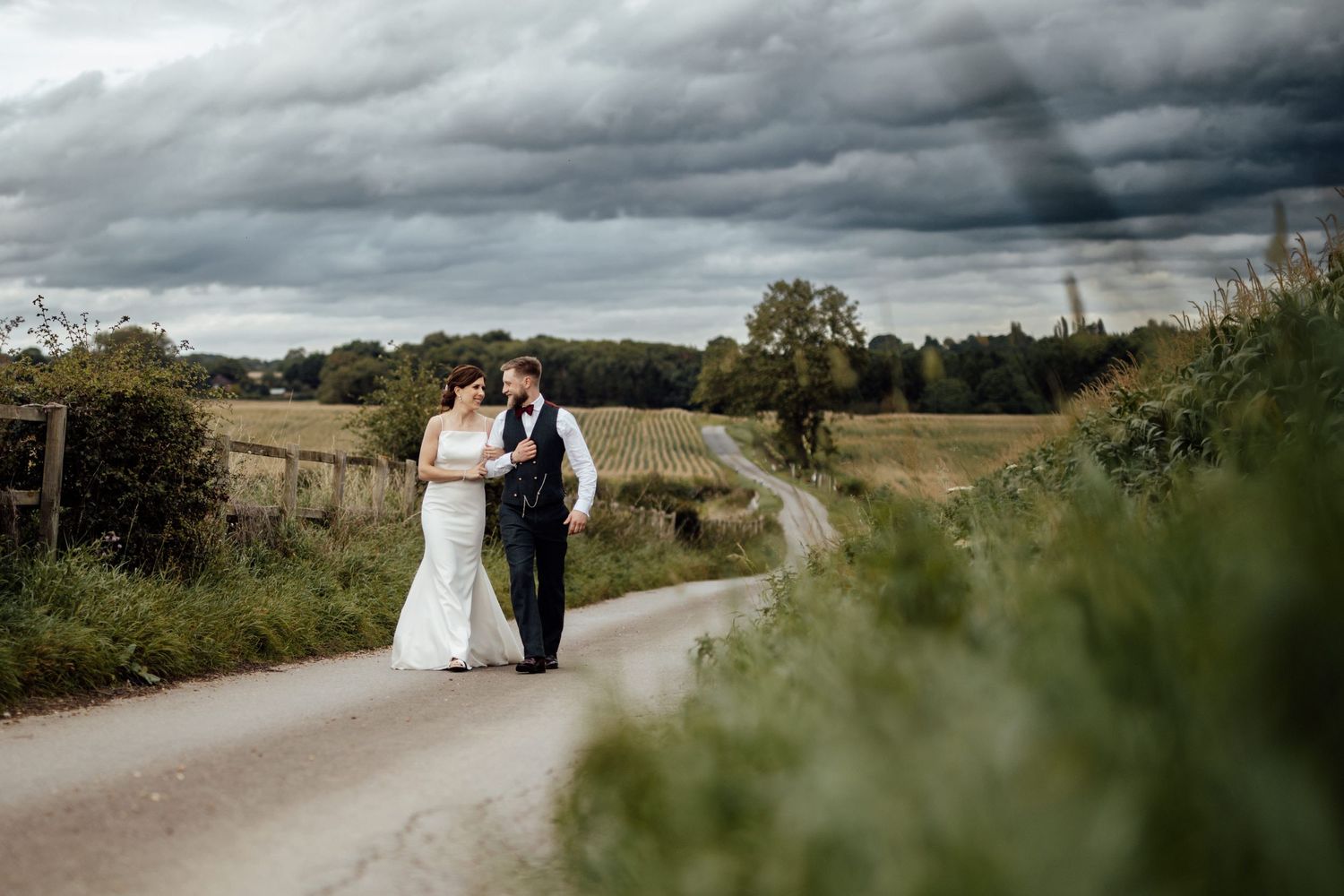 Wedding couple walks along a country road under dramatic cloudy skies.