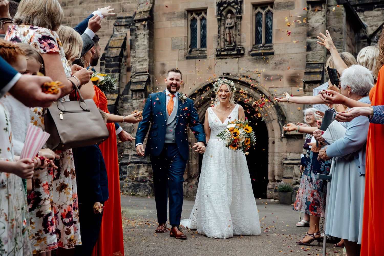 Wedding party exits church while guests throw confetti in celebration.