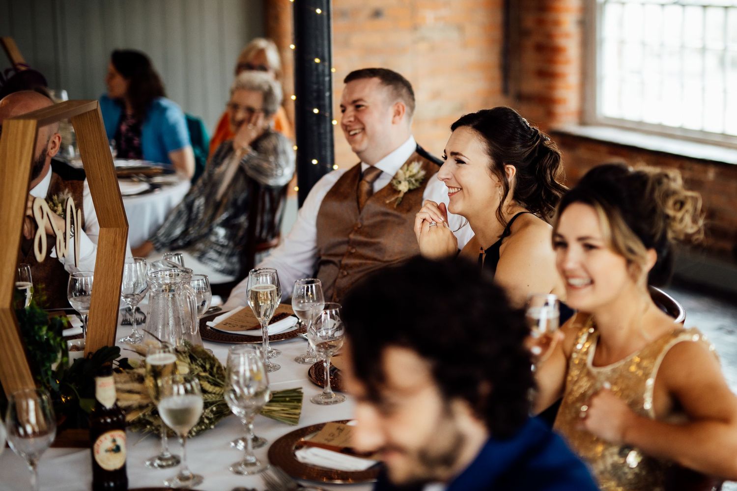 Wedding guests enjoying a lively reception dinner at rustic venue with exposed brick walls.