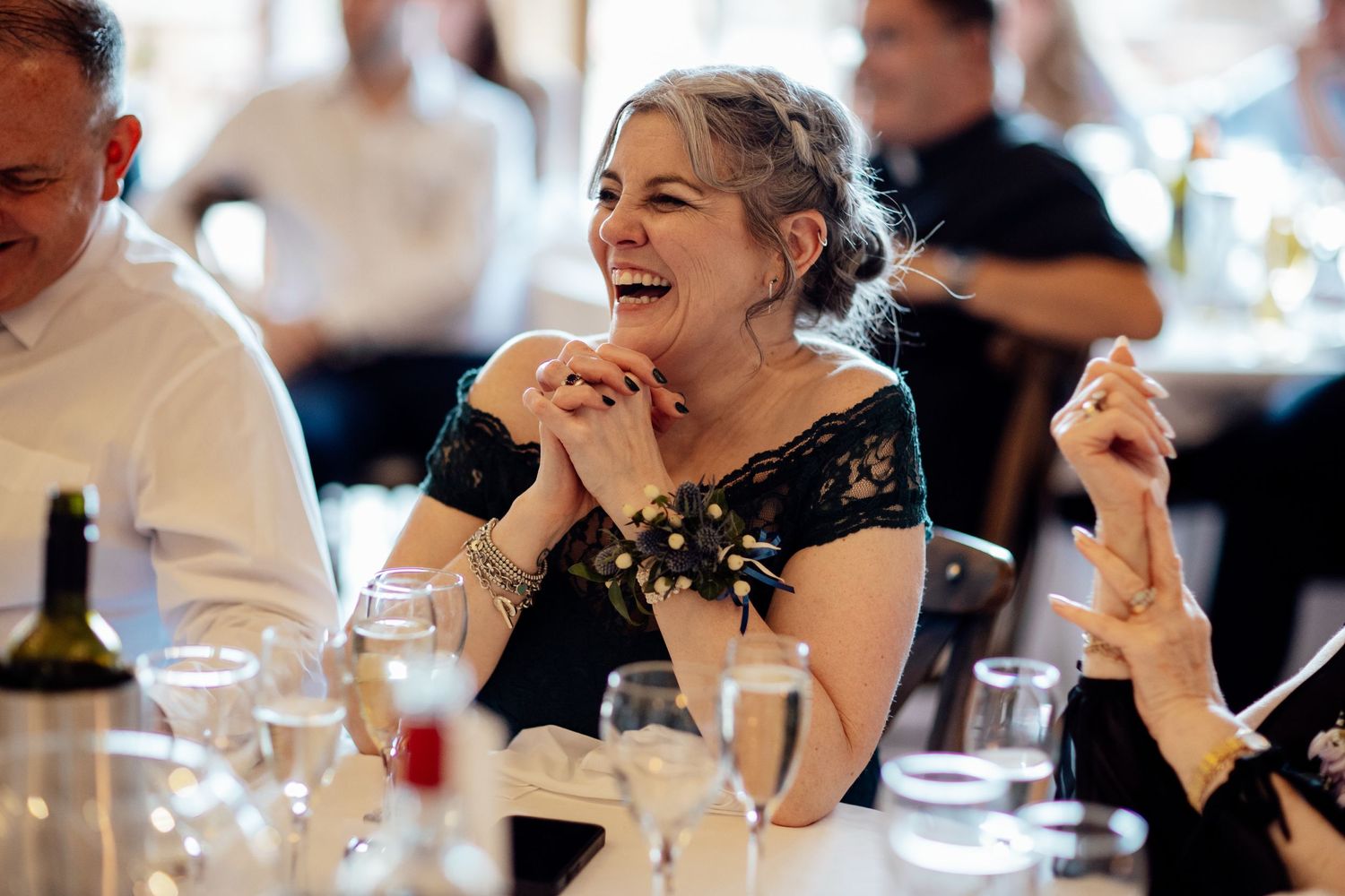 Wedding guests laugh and smile during a joyful reception celebration at an indoor venue.