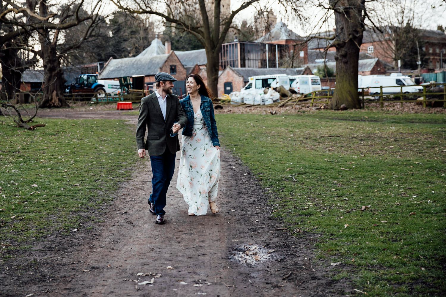A couple walks along a dirt path in a park setting with trees in the background.
