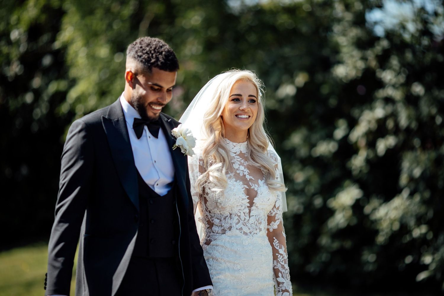 Elegant wedding couple walking together in a lush outdoor setting.