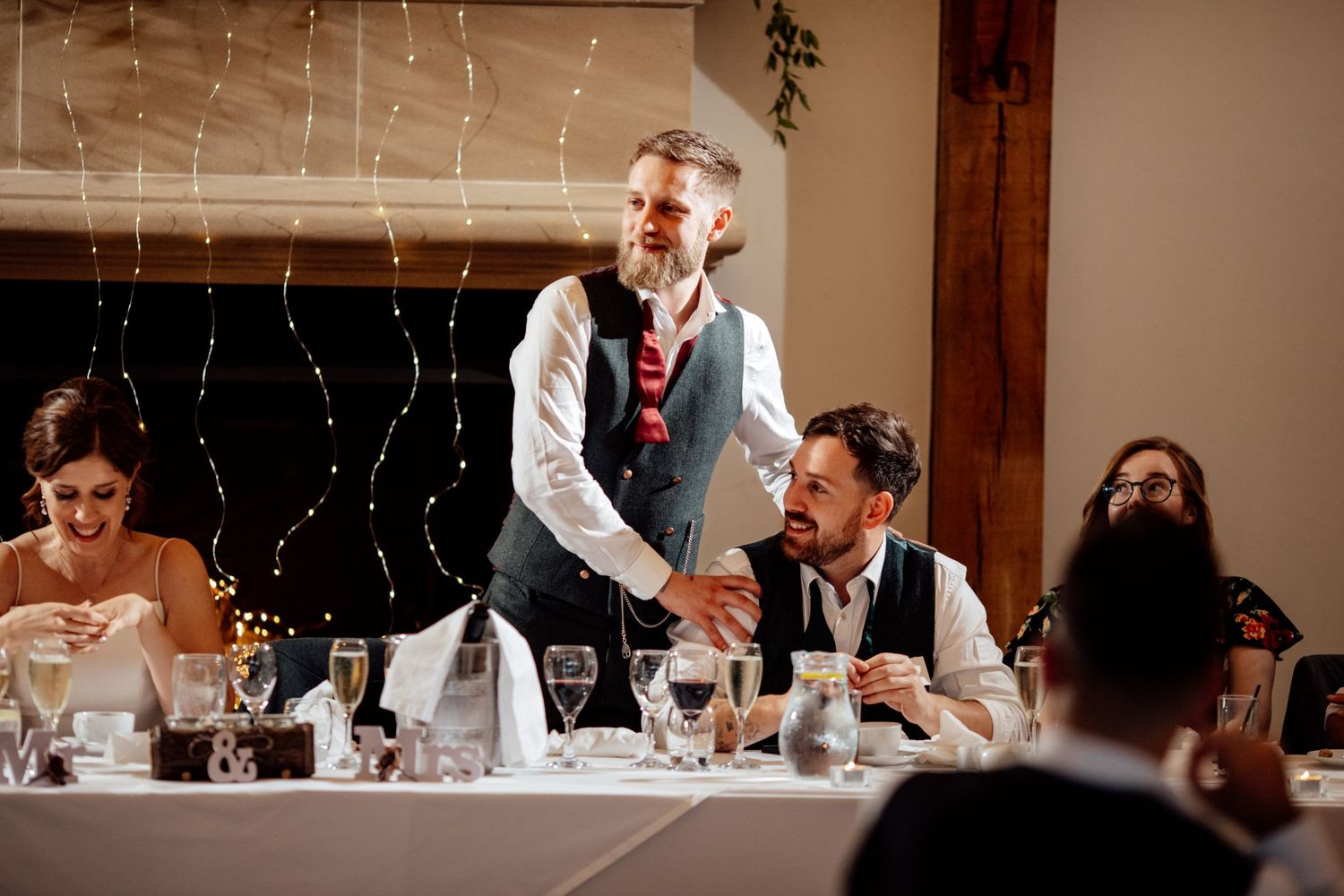 Wedding reception dinner setup with string lights and wooden beams creating an intimate atmosphere.