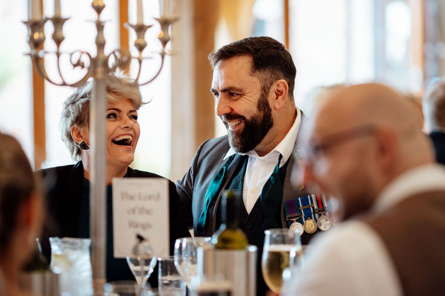 Wedding reception dinner scene with chandelier and natural window lighting.