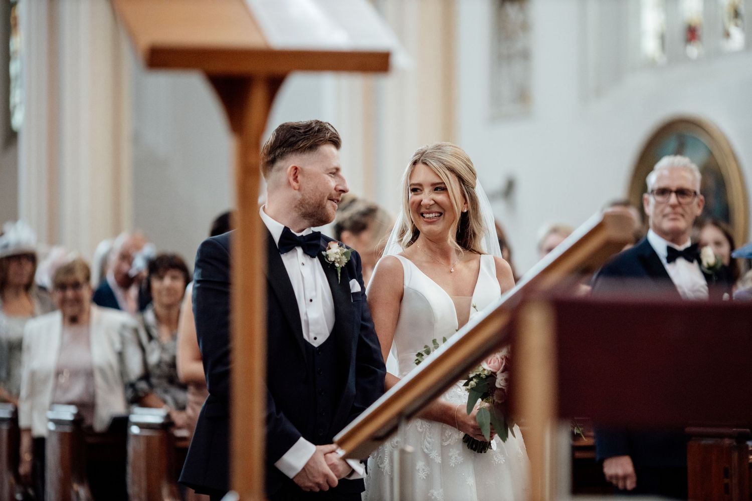 Wedding ceremony takes place in an elegant white church interior.