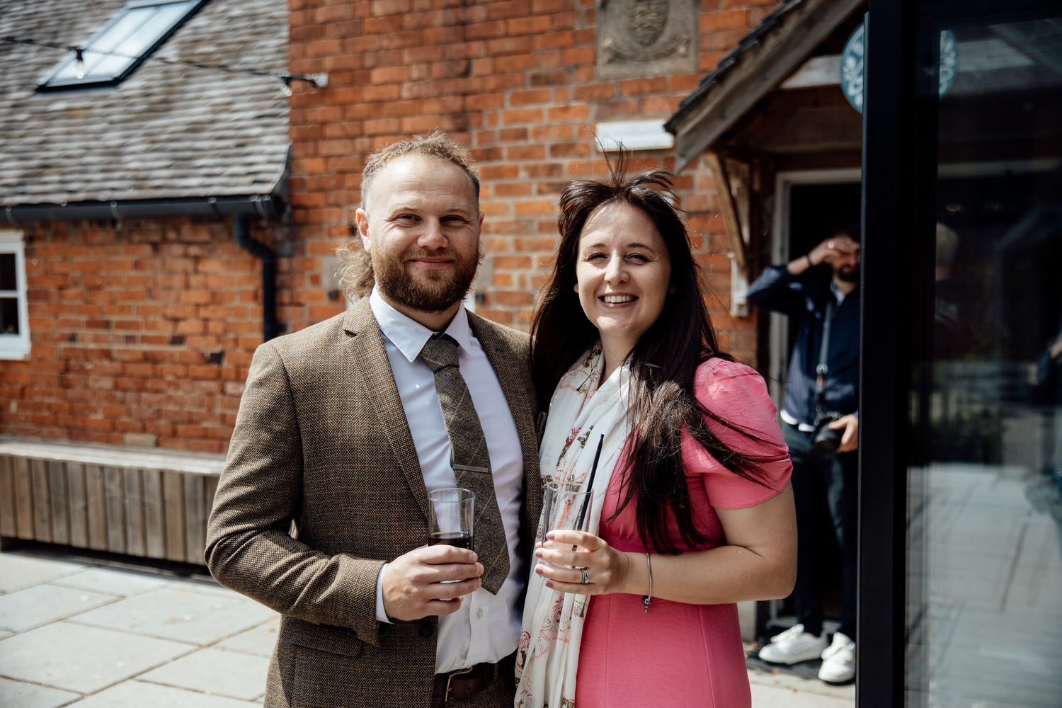 Wedding guests enjoying drinks and conversation outside a rustic brick venue.