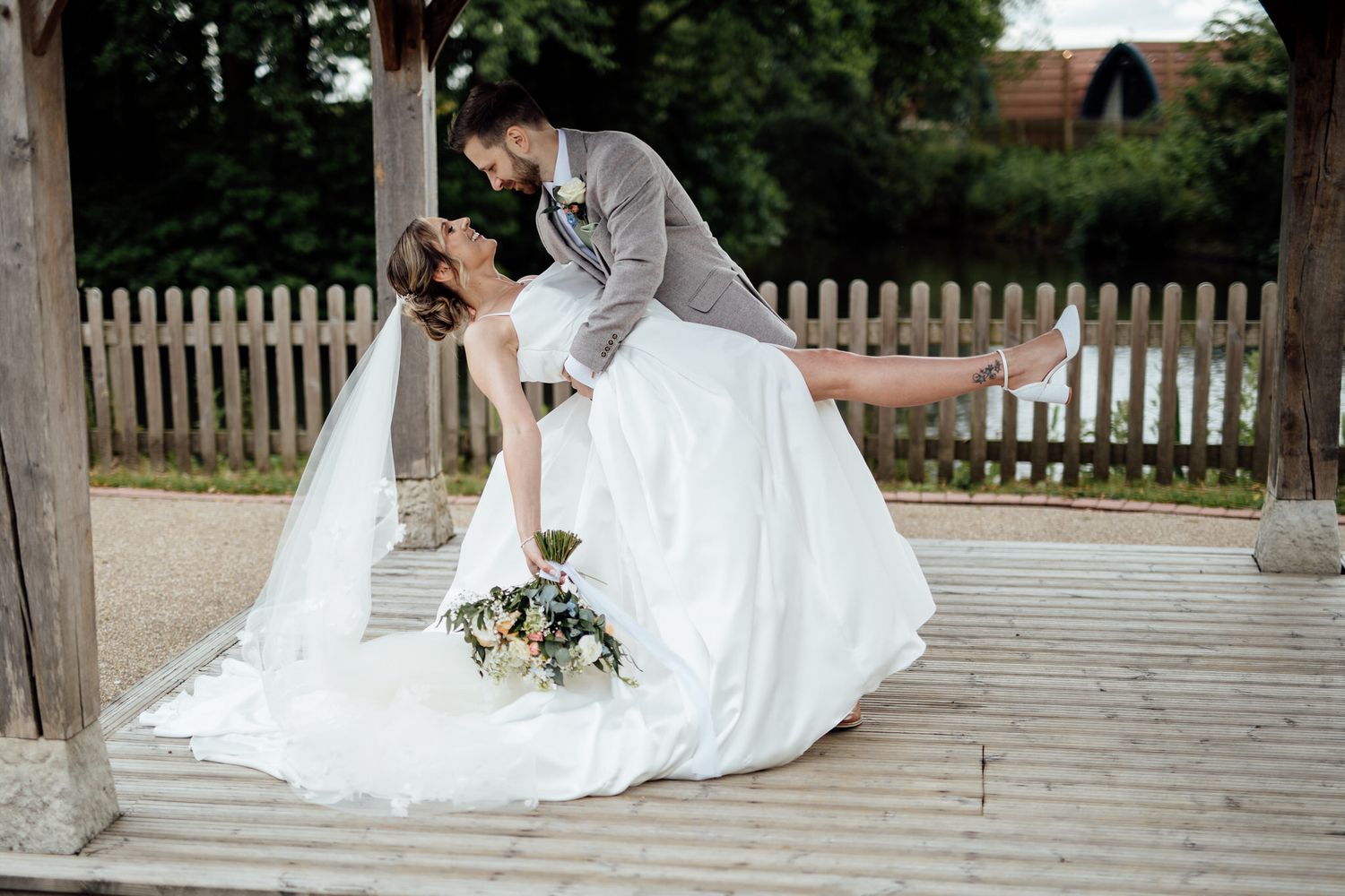 A romantic wedding portrait on a wooden deck with a dramatic dip pose.