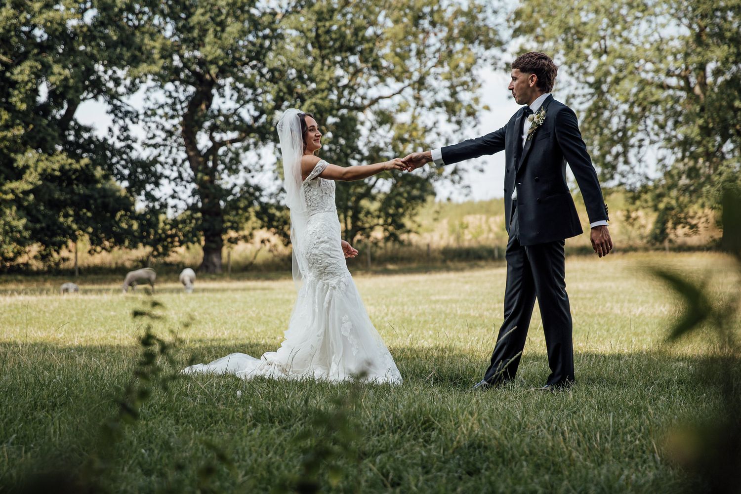 Wedding couple walking through a sunlit grassy field during outdoor photo session.