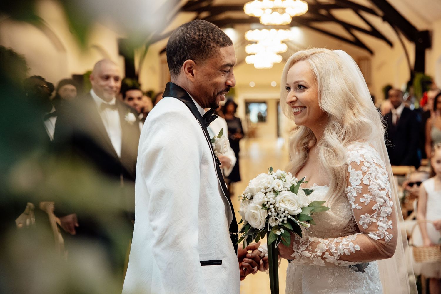 Interracial couple sharing a joyful moment at the wedding altar, bride holding a white floral bouquet.