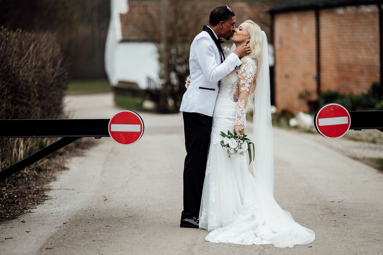 Bride and groom sharing a kiss on a road flanked by no-entry signs.