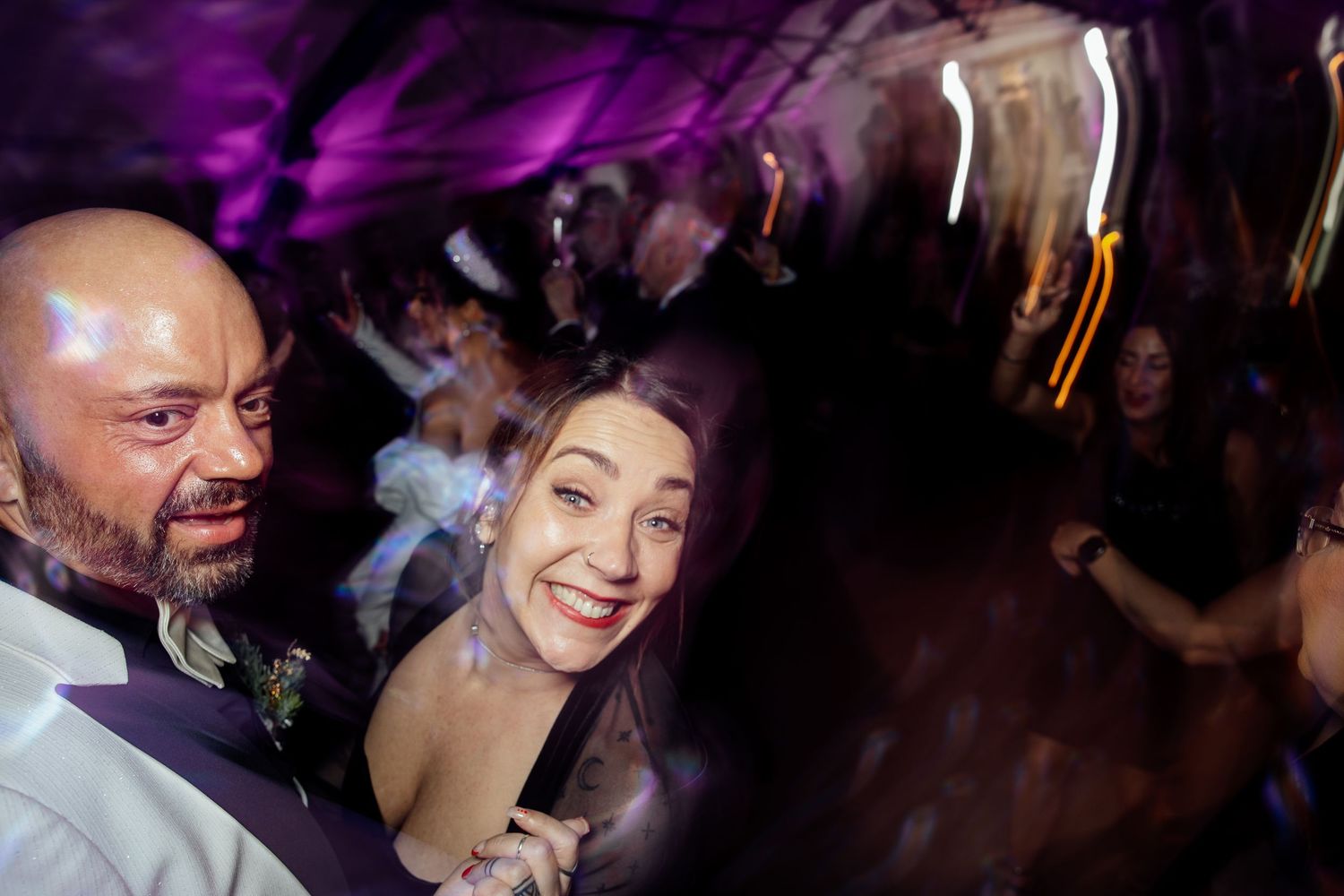 Wedding reception dance floor filled with guests under vibrant purple lighting.