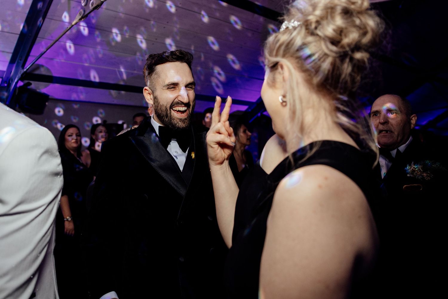 Dance floor filled with wedding guests under purple mood lighting.