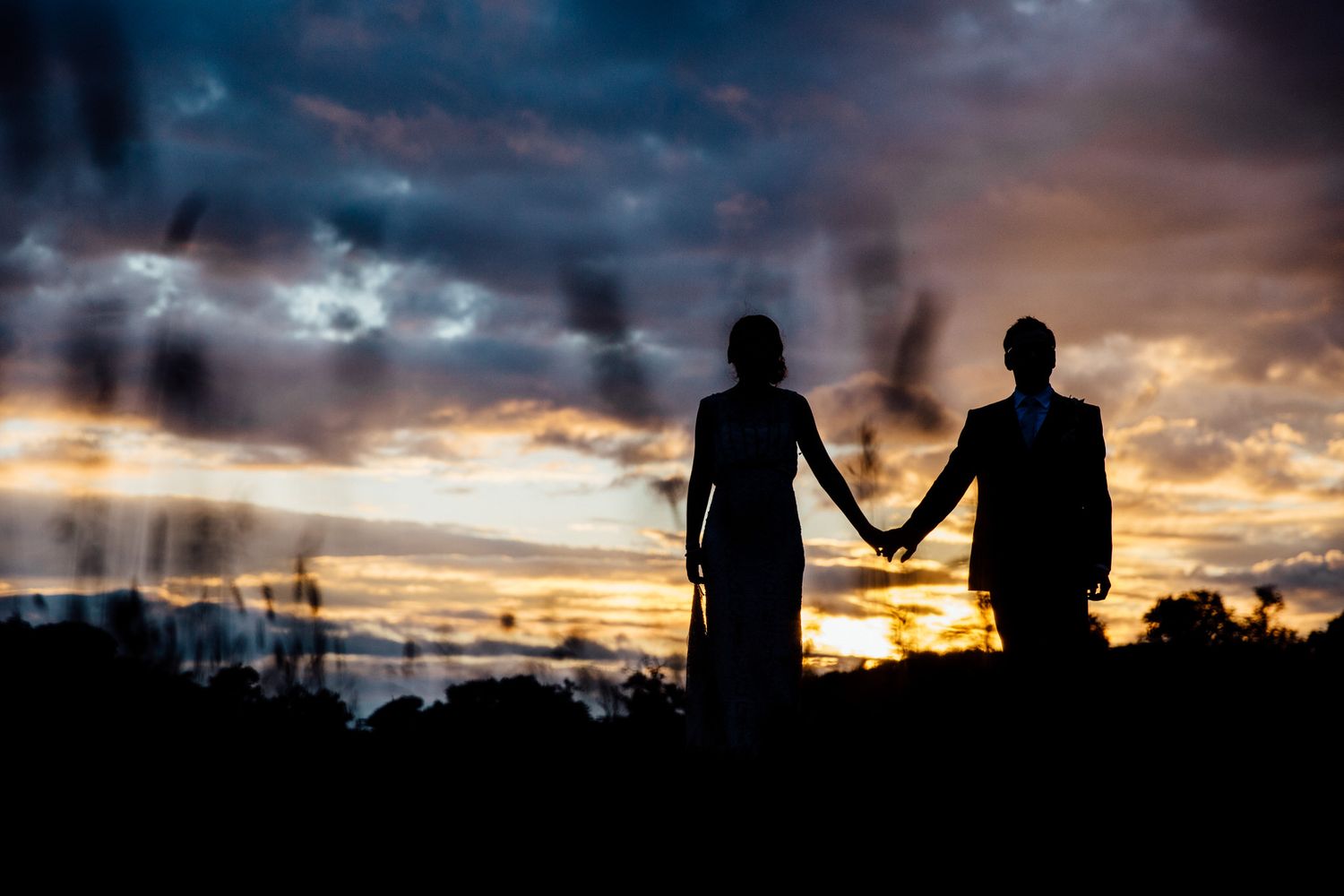 Silhouette of a couple holding hands against a dramatic sunset sky.
