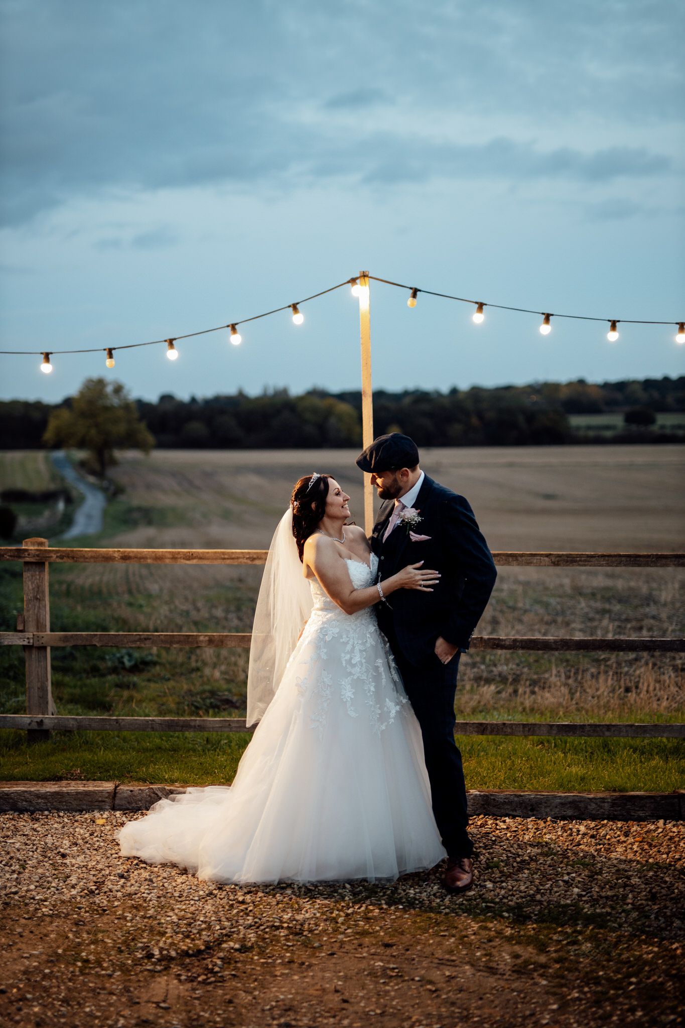 Evening wedding portraits under string lights with rolling hills in background.