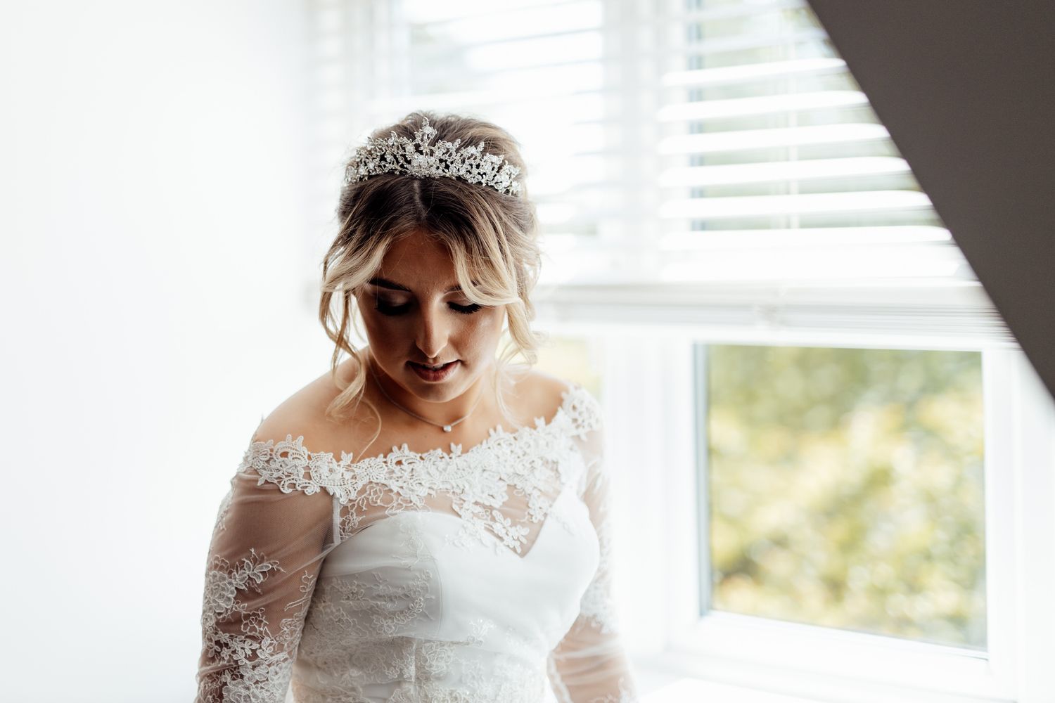 Close-up details of delicate lace on a white wedding dress near a window.