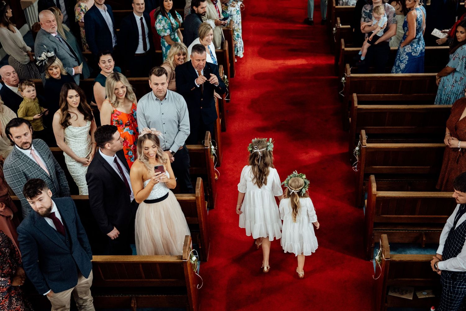 Wedding ceremony procession in a church with red carpet and wooden pews.