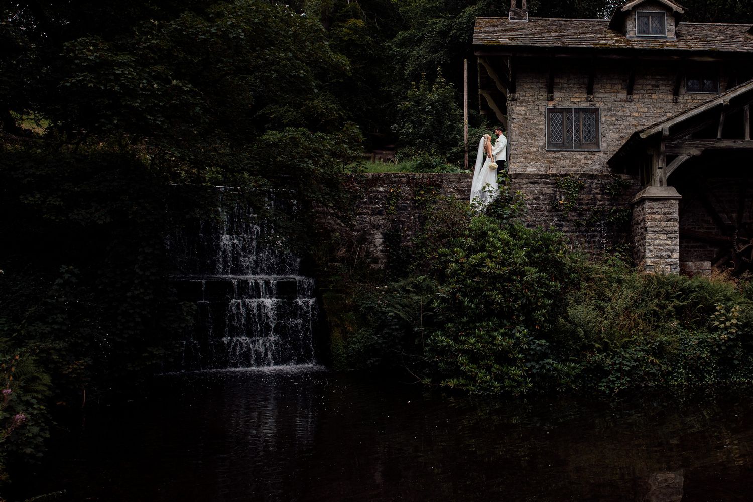 Stone building with cascading waterfall and lush greenery creates a romantic backdrop.