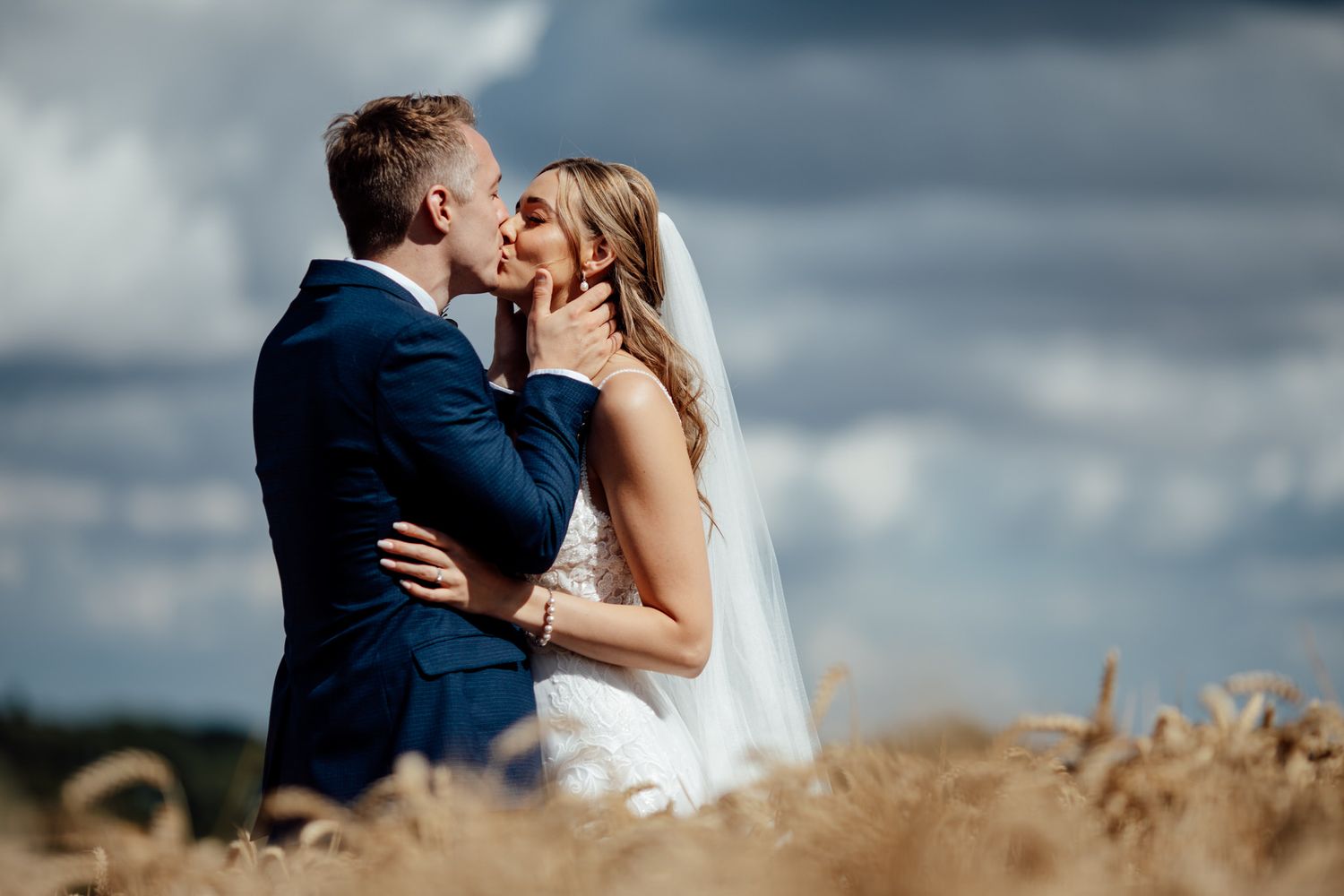 A romantic moment captured in a wheat field under dramatic clouds.