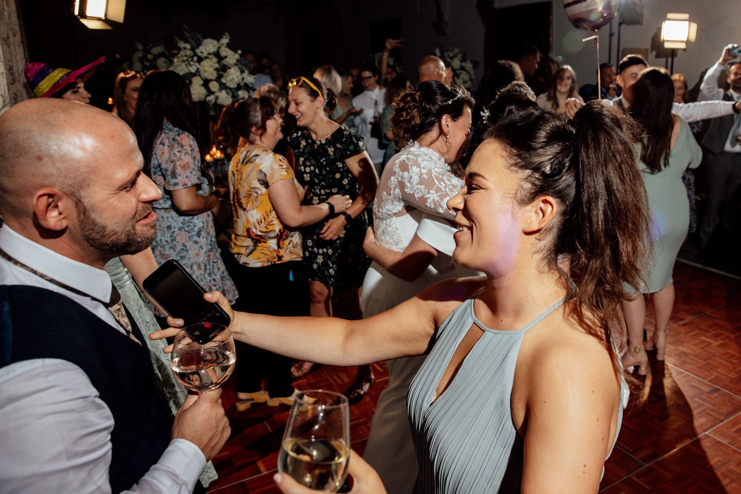 Lively wedding reception with guests dancing and celebrating in a dark venue with ambient lighting.