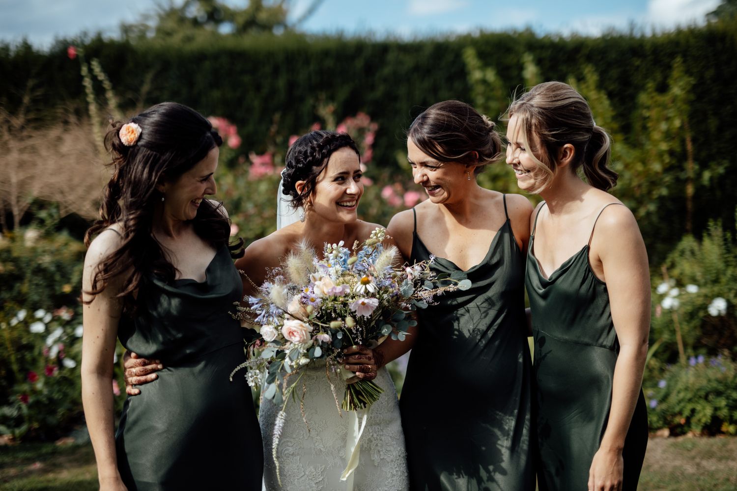 Wedding party in black dresses holding white flower bouquets in an outdoor garden setting.