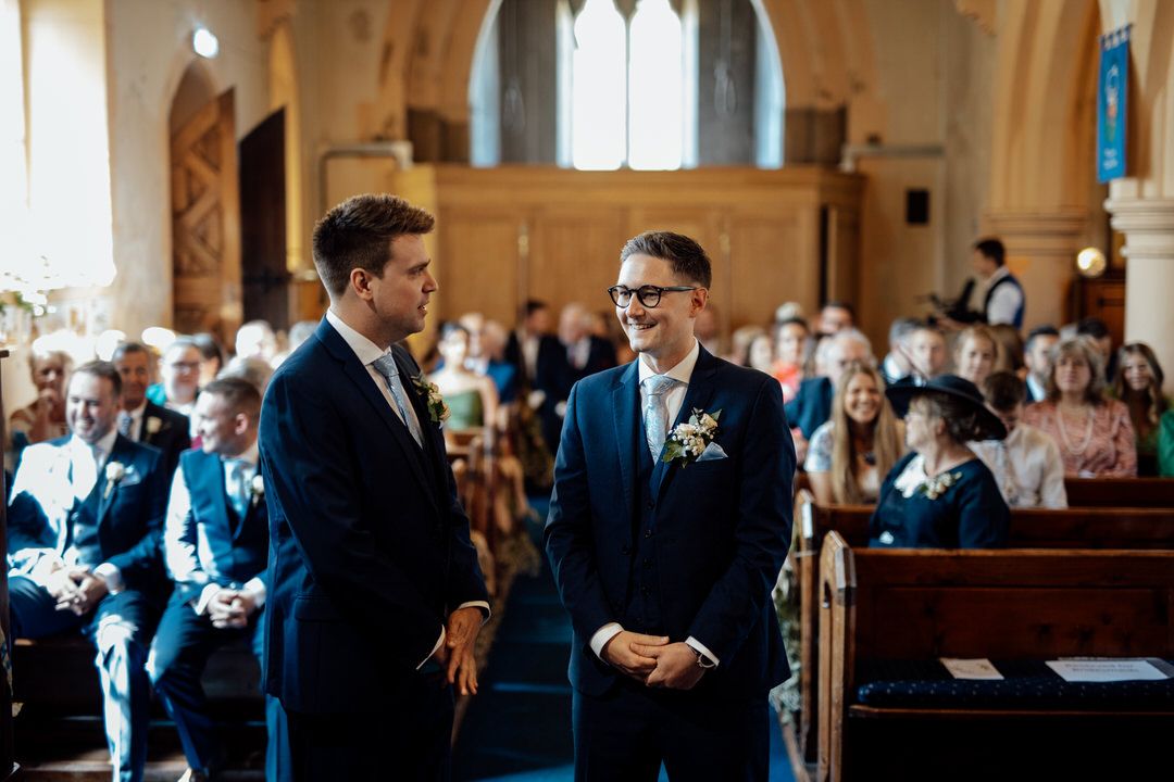 Church interior with wooden pews and arched windows during wedding ceremony.