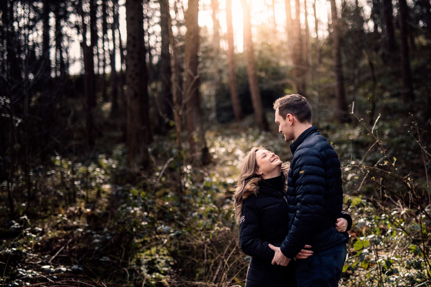 Couple enjoying a tender moment in a sunlit wooded area during autumn.