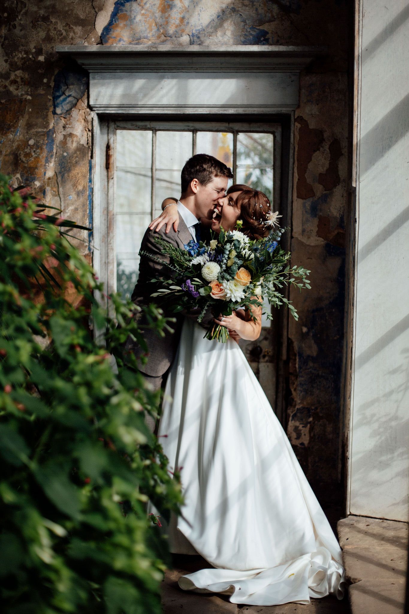 Romantic wedding portrait in a rustic doorway framed by greenery and stone walls.