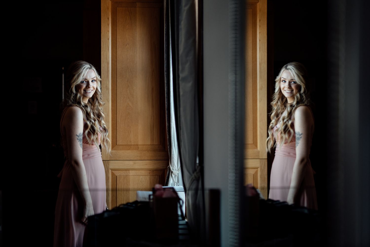 Two people in white and pink outfits stand in a dimly lit room with natural window light.