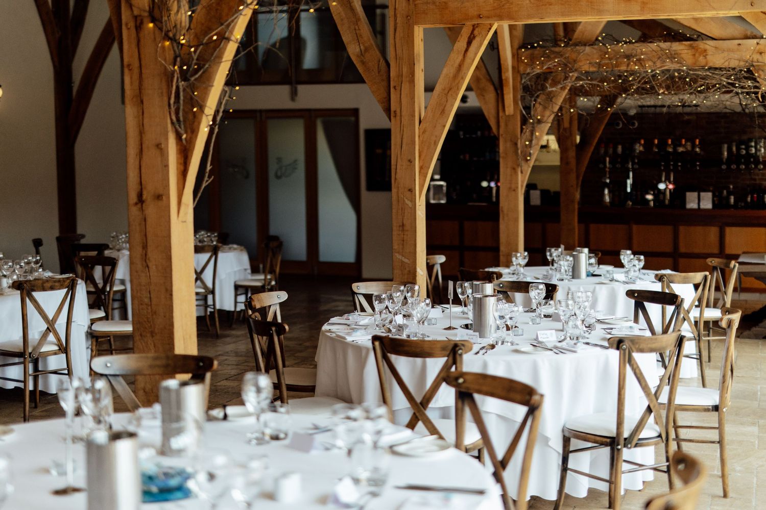 Rustic barn venue with wooden beams and elegant table settings for a wedding reception.