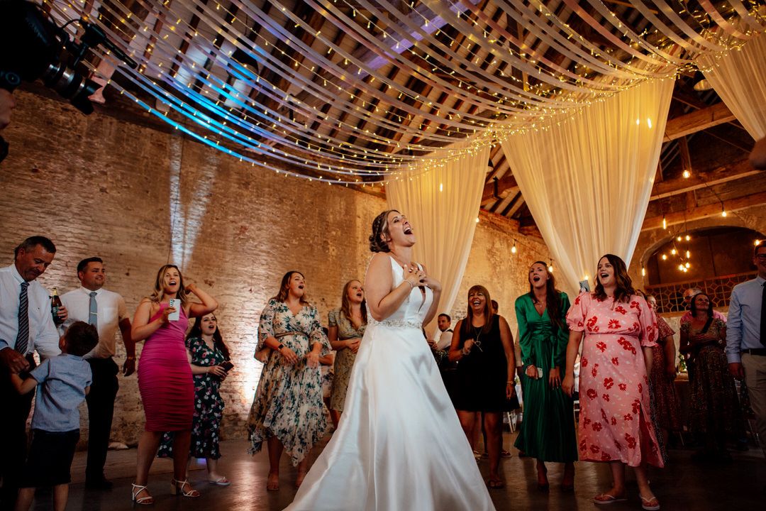 Wedding reception dance floor panorama showing guests celebrating under string lights and white drapes.