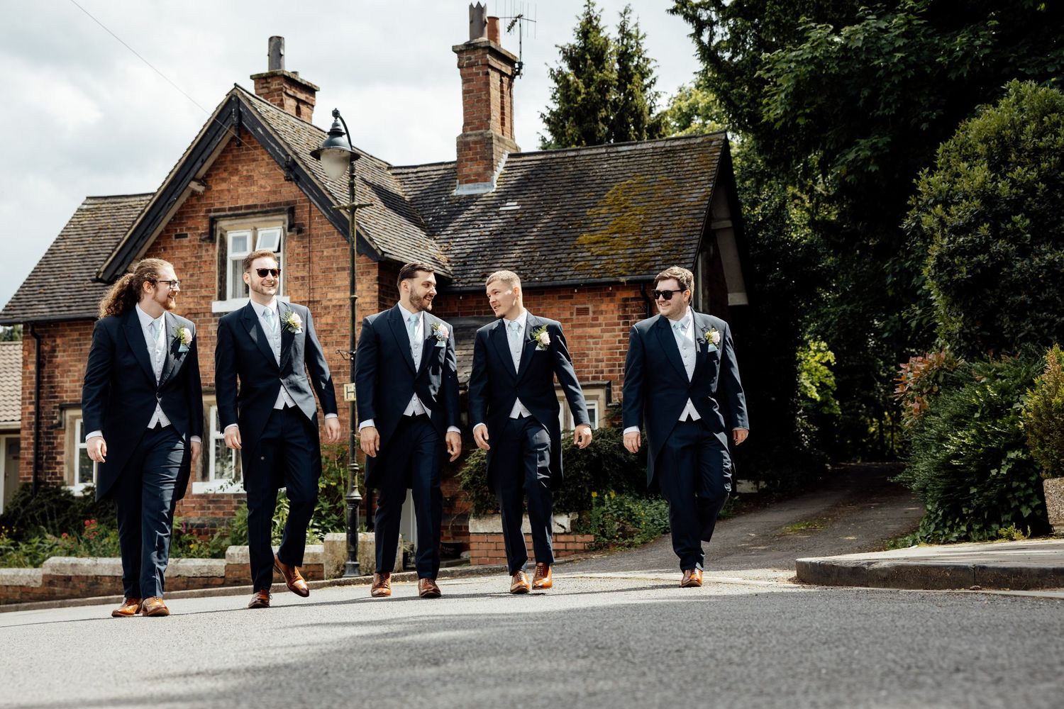 Groomsmen walking together in navy suits along stone path near brick buildings.