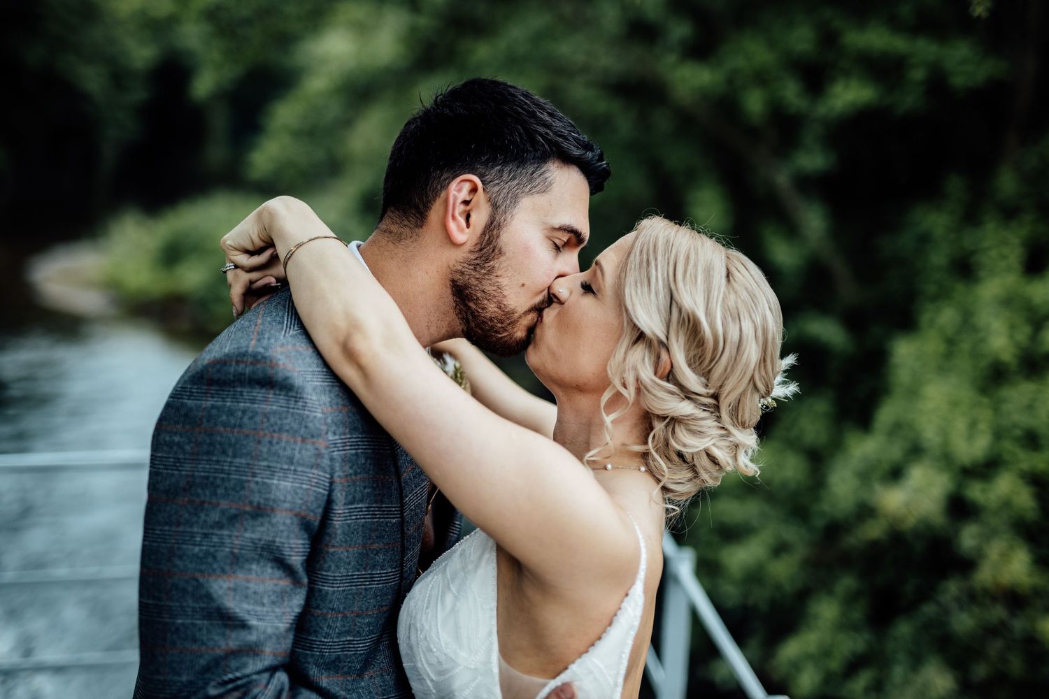 Romantic wedding couple embracing outdoors with lush greenery in background.