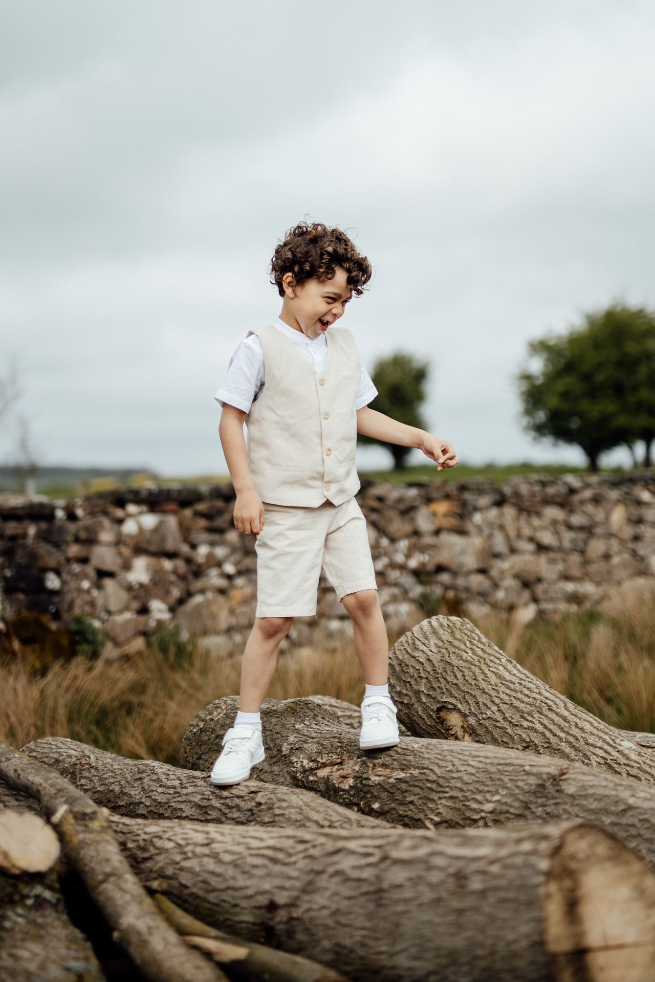 A child in cream-colored clothing explores a fallen log in an outdoor setting.