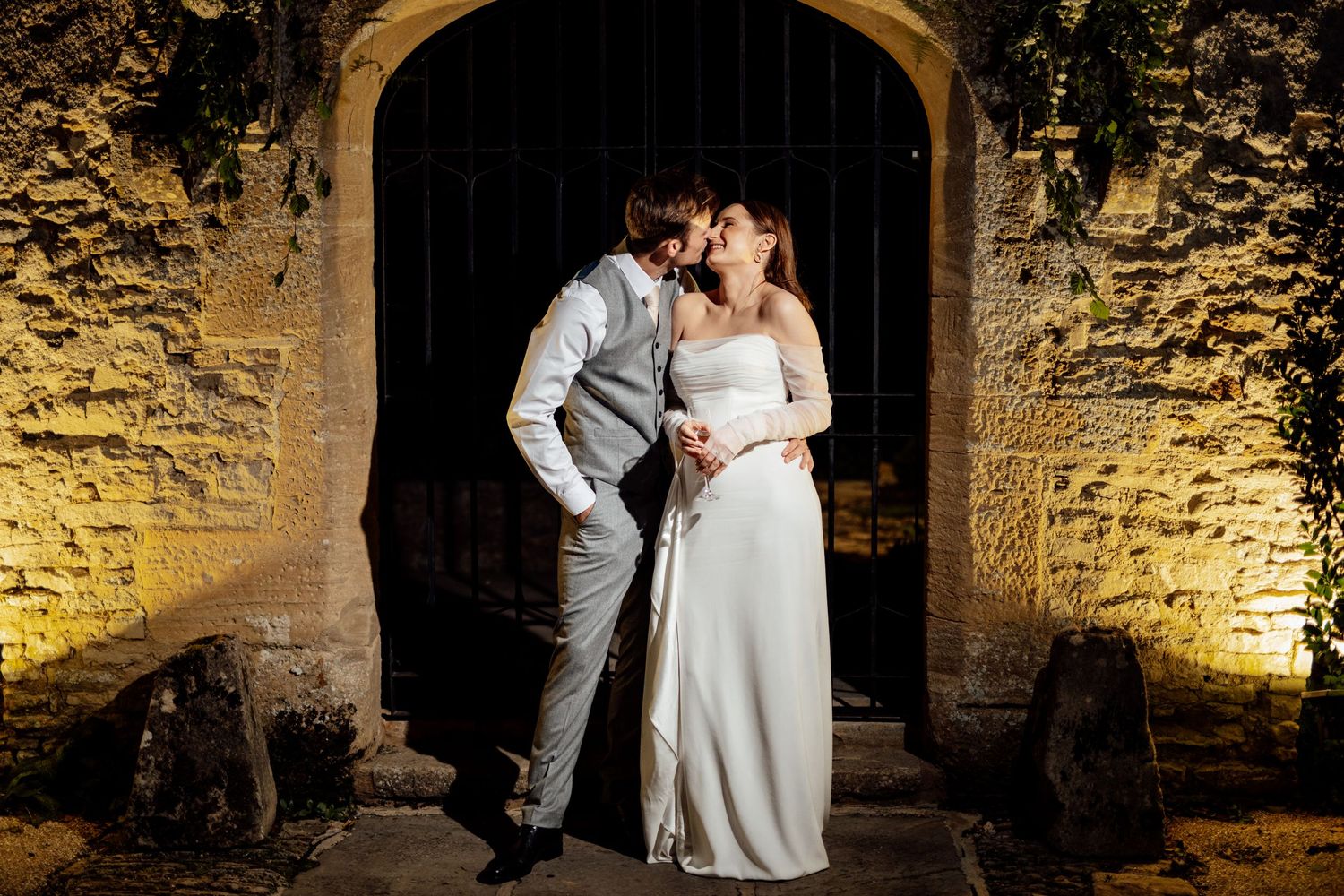 A romantic evening portrait of newlyweds in front of an illuminated stone archway.