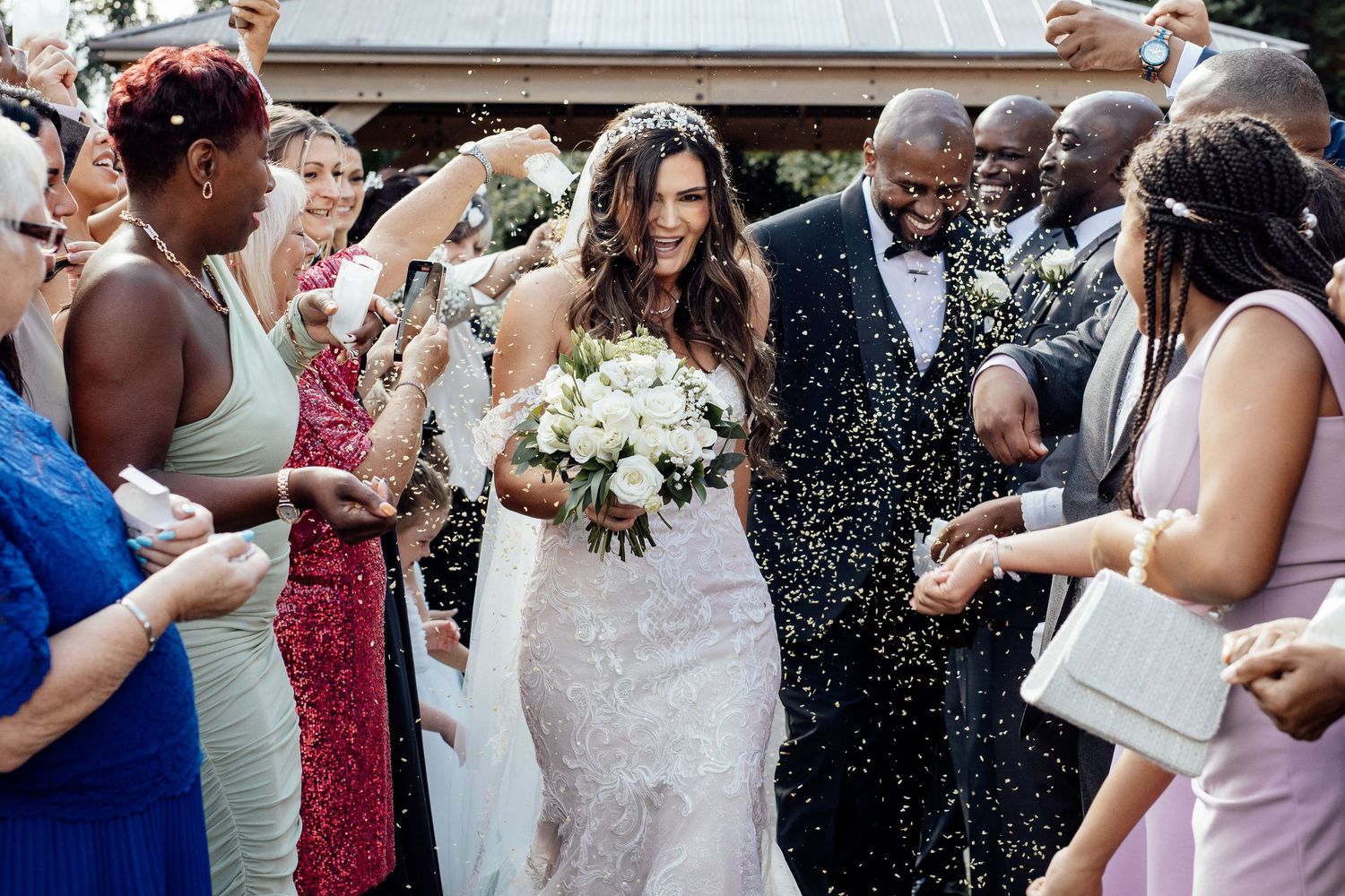 Wedding guests celebrate with confetti and laughter at an outdoor ceremony.