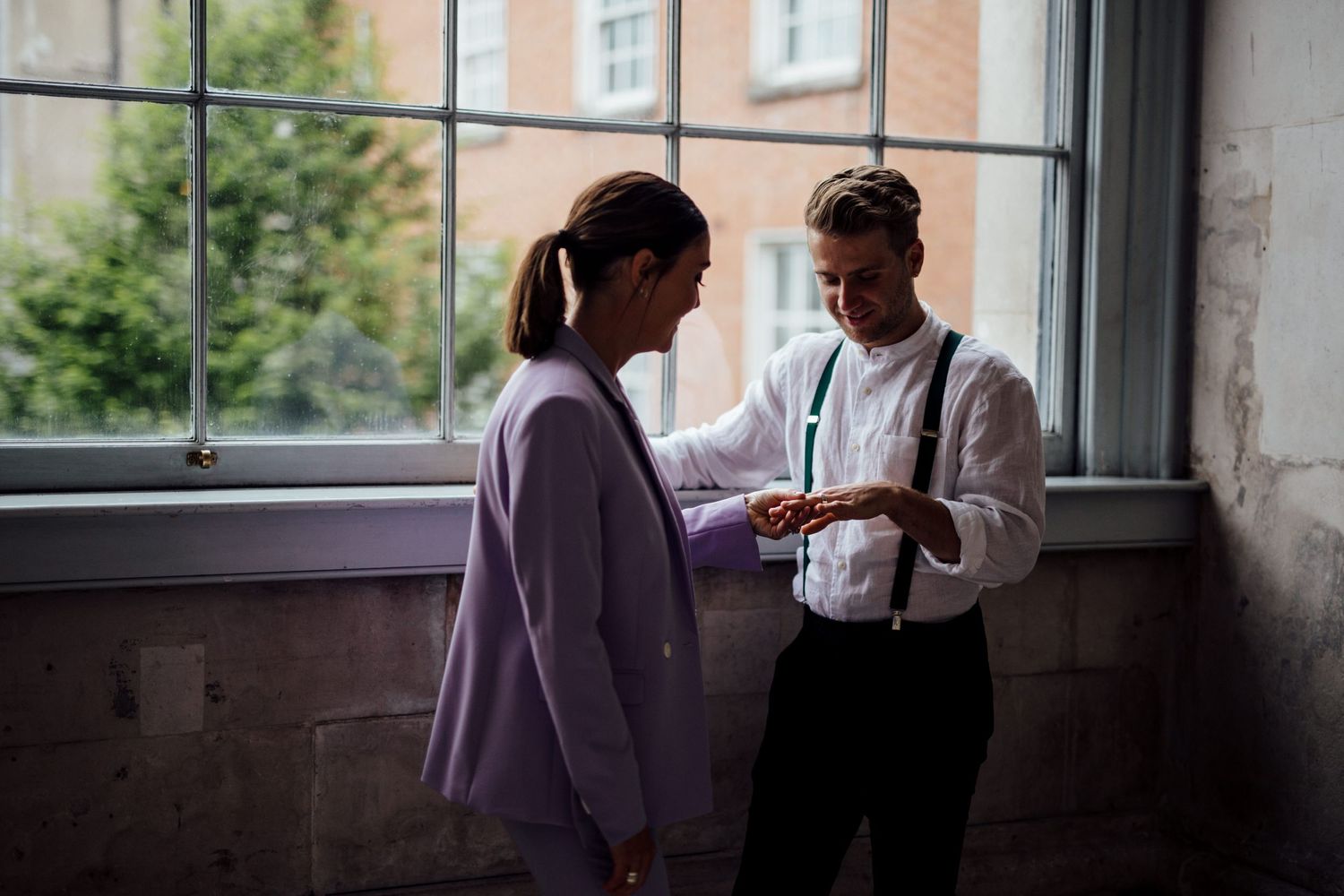 A silhouetted couple stands by large windows in natural light.