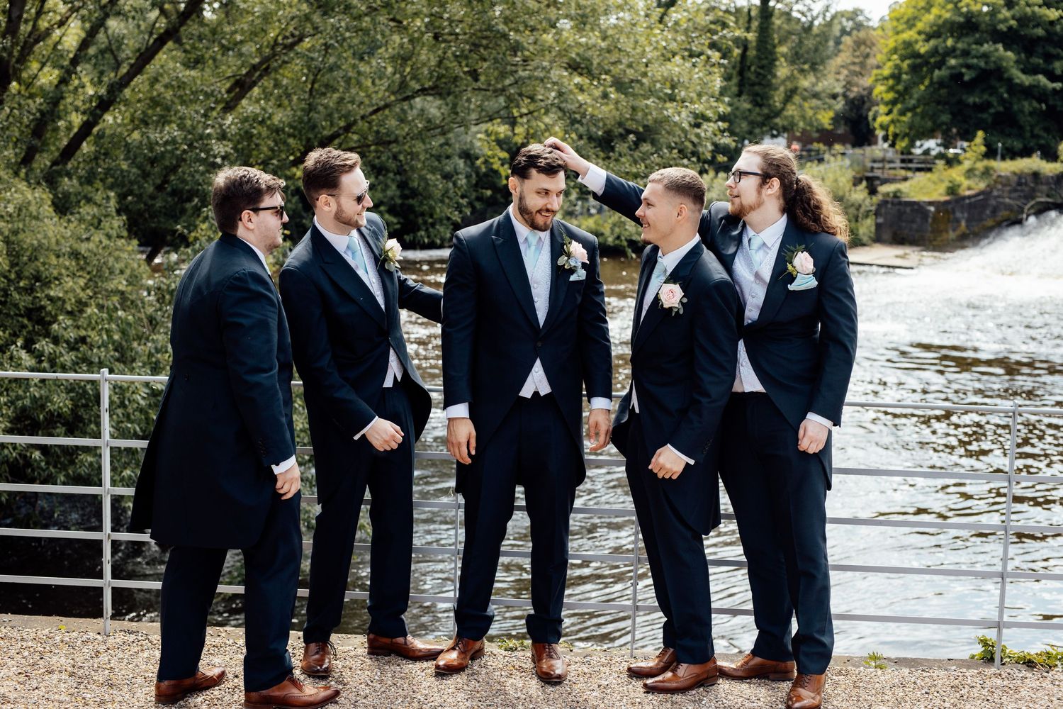 Groomsmen in navy suits standing along waterfront railing.