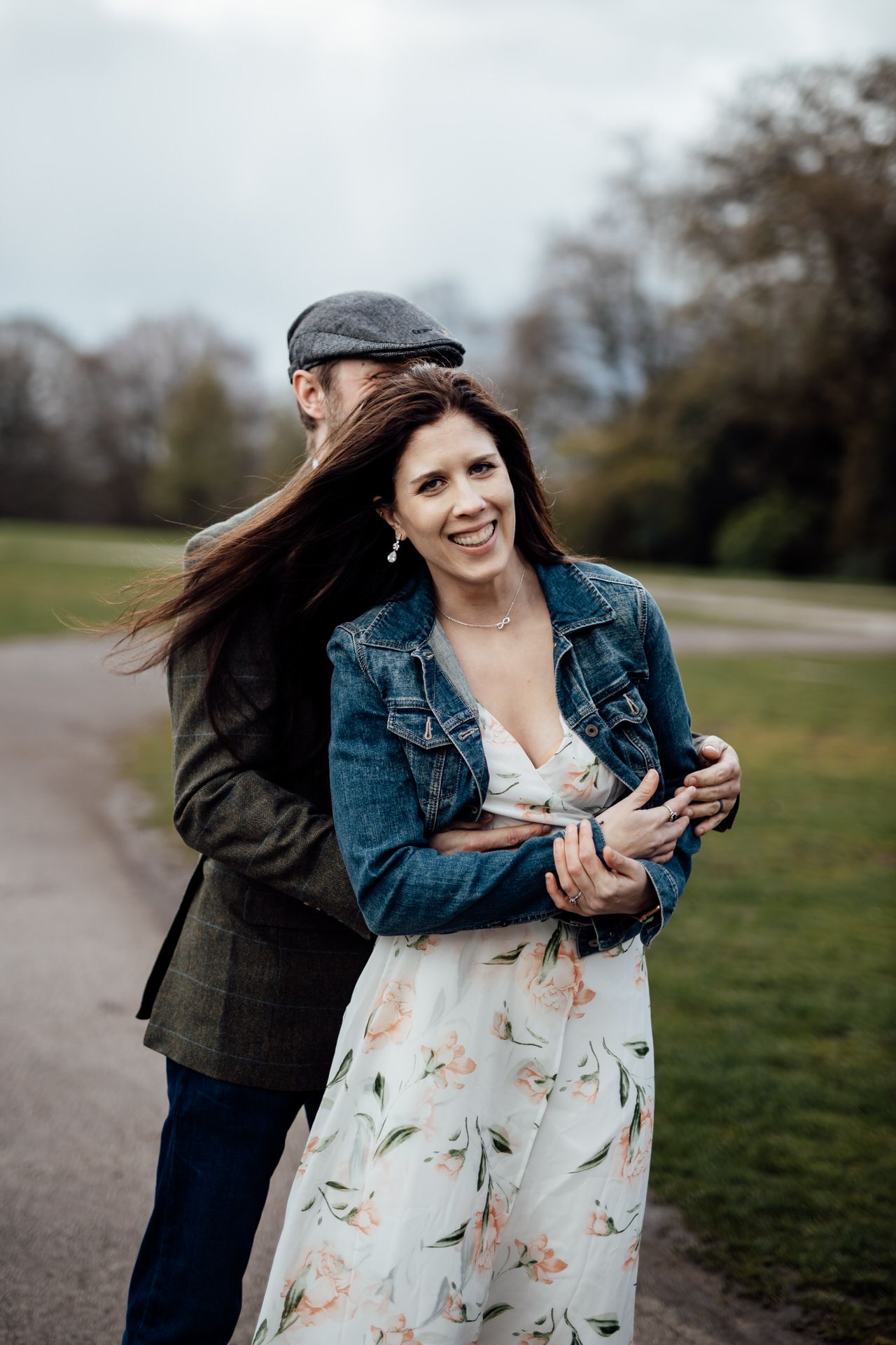 A couple shares a playful moment outdoors with the person in a floral dress and denim jacket laughing joyfully.