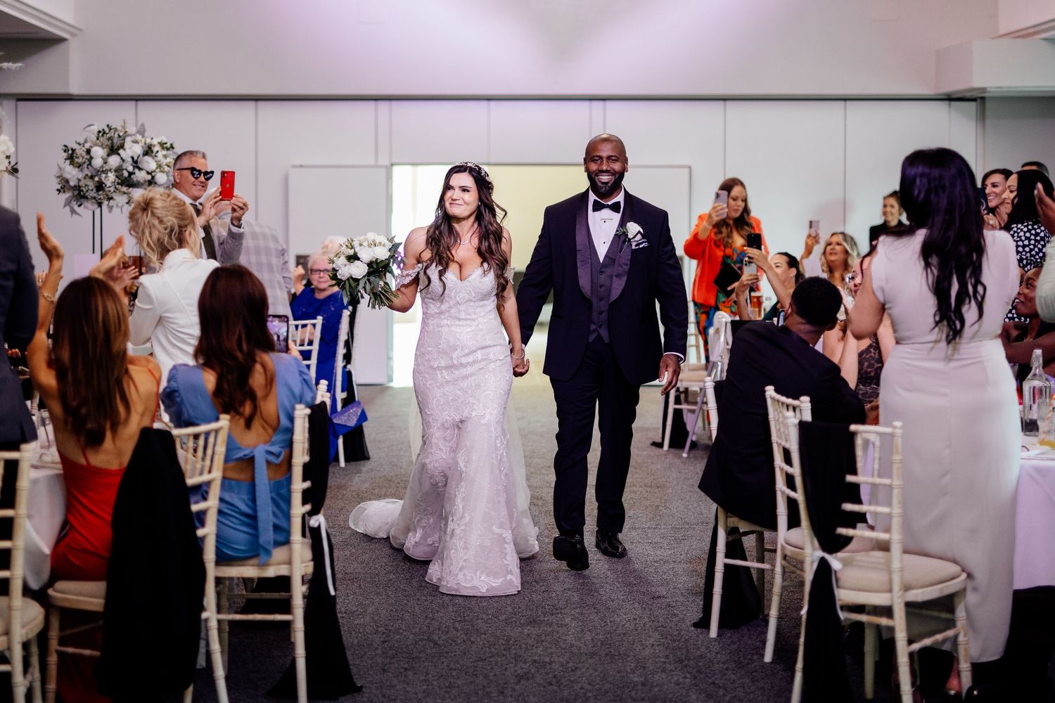 Newlyweds walking down the aisle while guests celebrate their union in a modern venue.