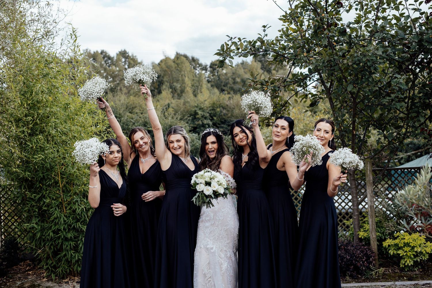 Bridal party in black dresses poses together for formal outdoor wedding photos.