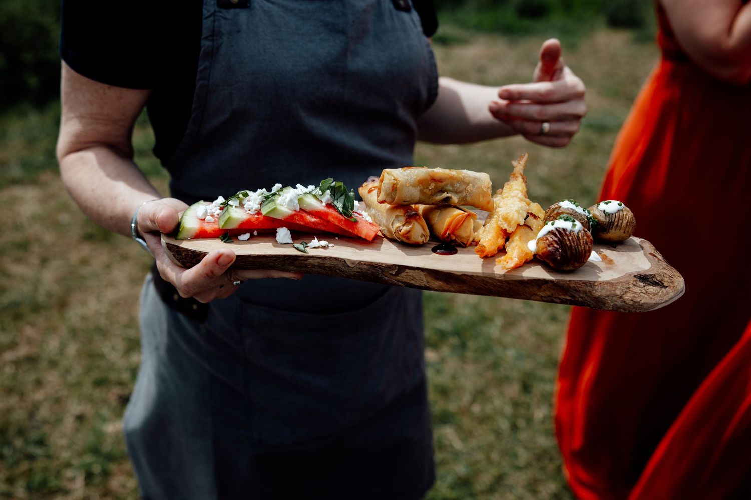Wedding reception food being served on wooden platters outdoors.