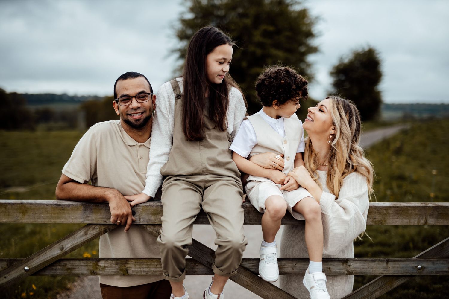 Family relaxing together on wooden fence in countryside setting.