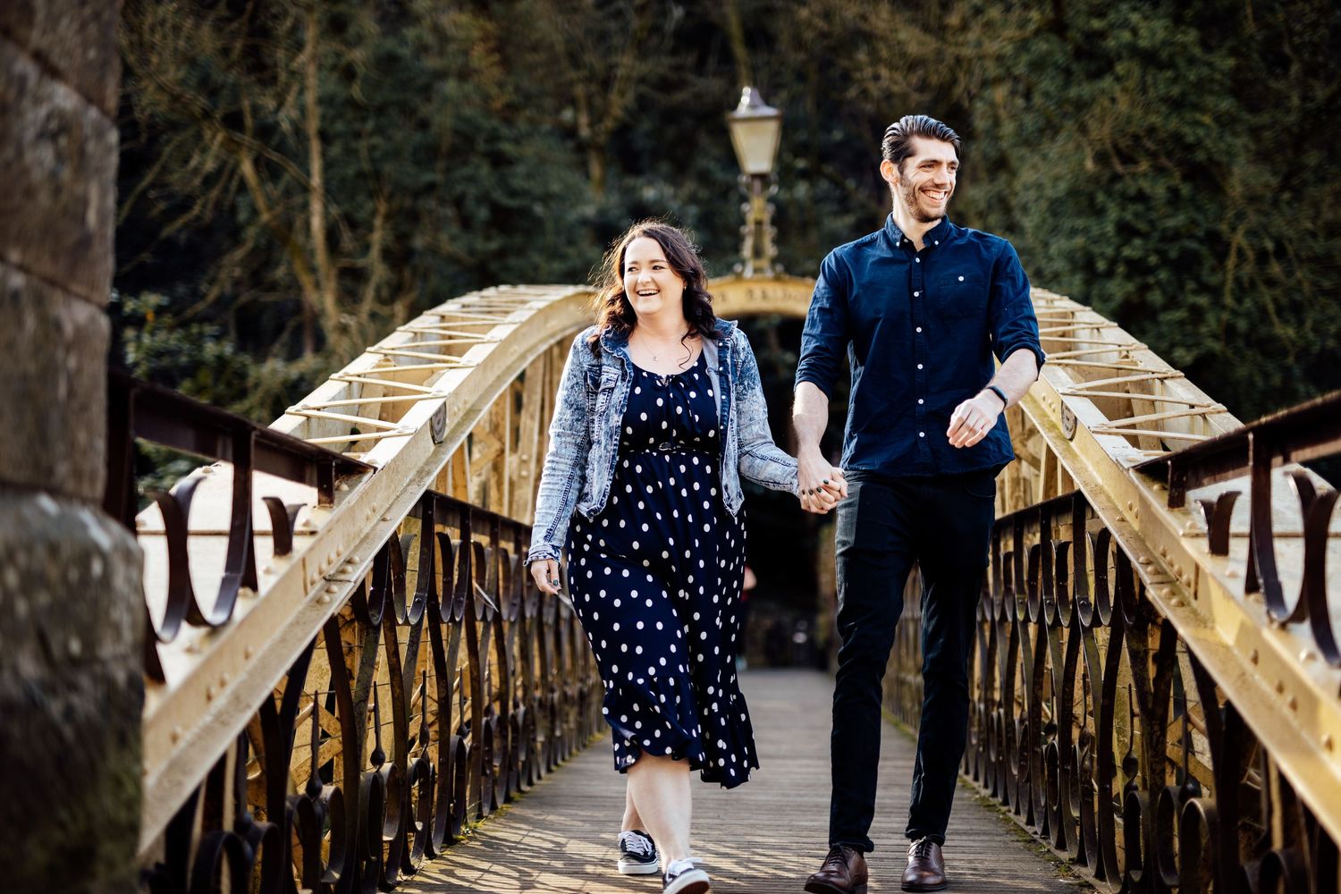 A couple walks together across a vintage wooden bridge in a park setting.