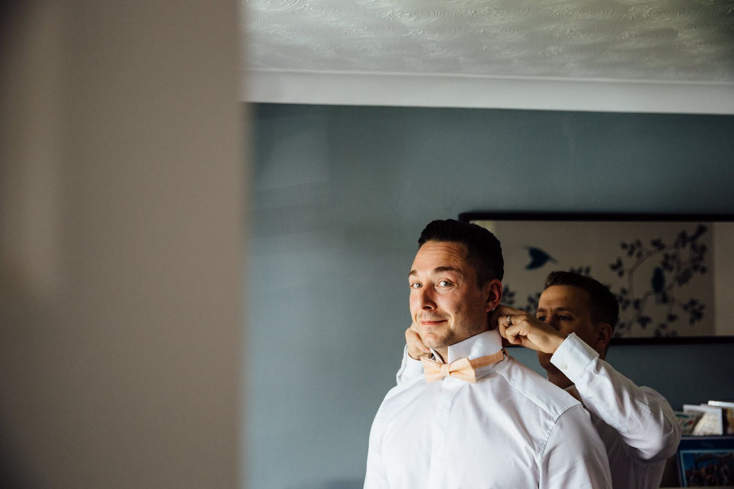 Wedding party members in formal attire stand together against a brick wall interior.
