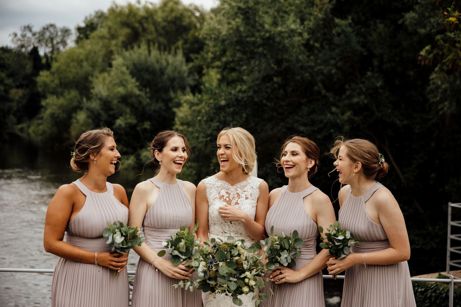 Bridal party in coordinated dresses posing together by waterfront.